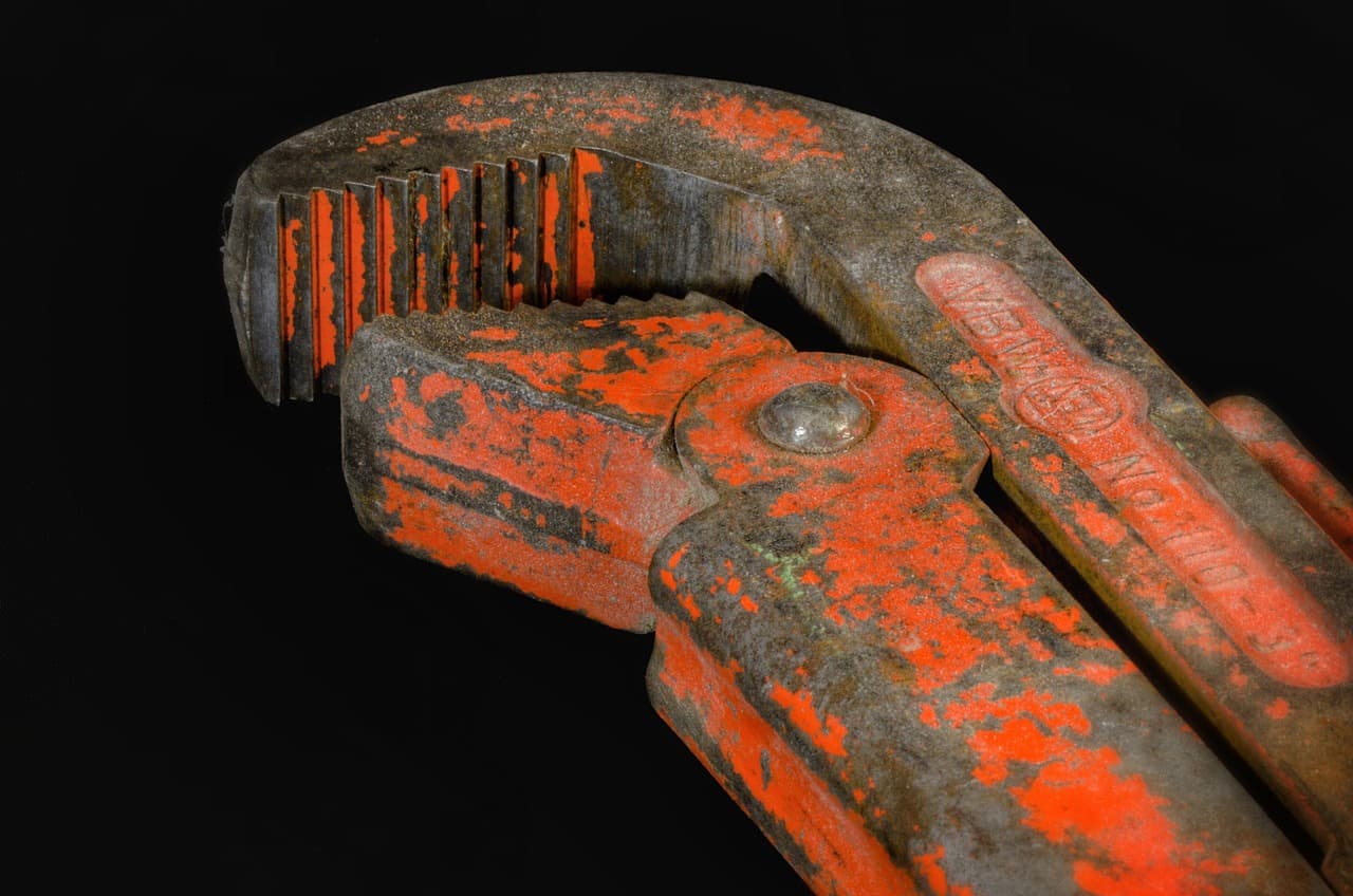 A well-used pipe wrench with chipped orange paint on a dark bench
