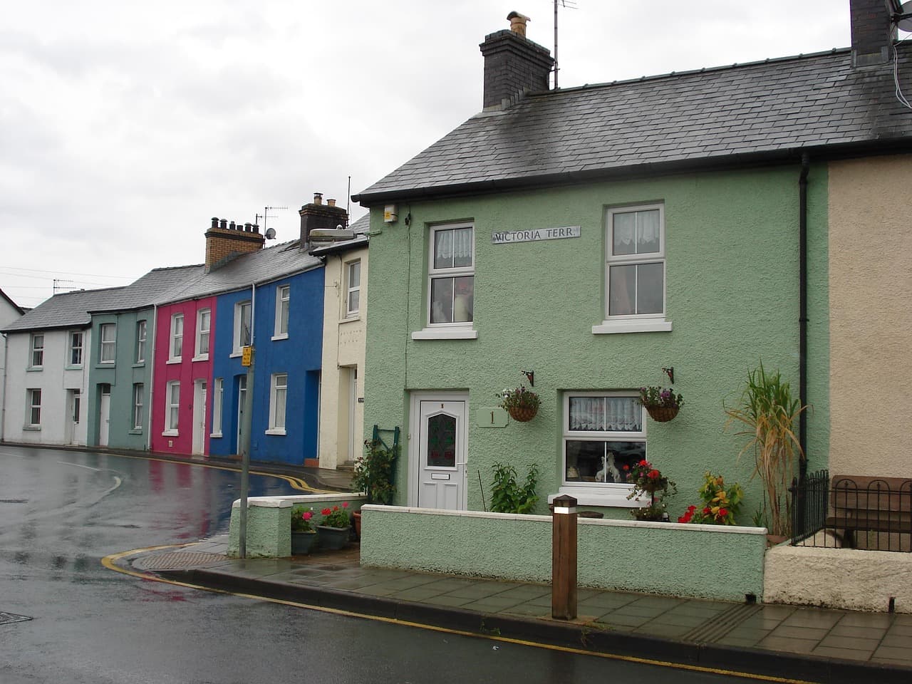 A wet terraced street in Wales: slate roofs, houses painted green, blue and pink, double yellow lines