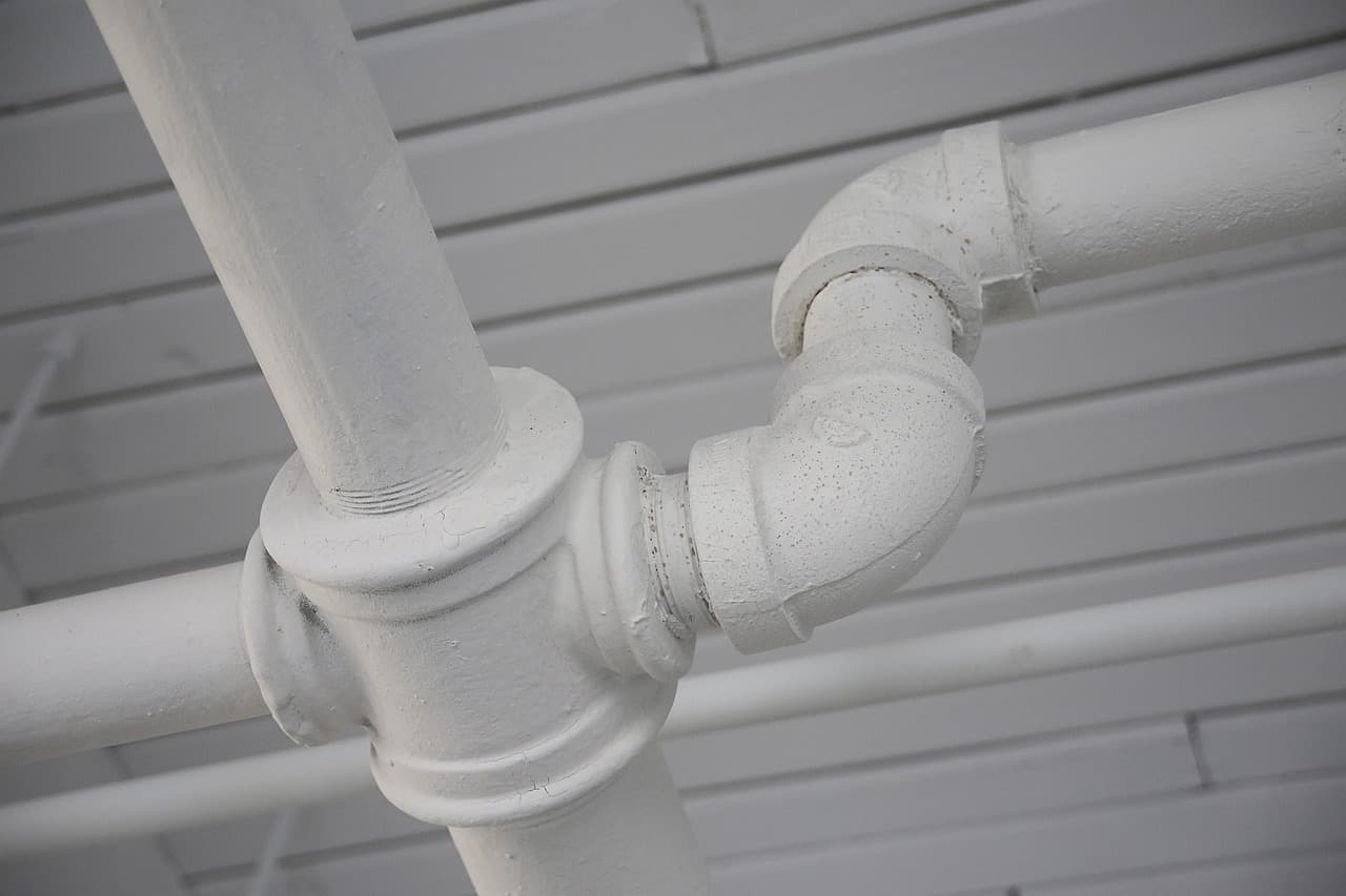 Painted water pipes and a compression bend fixed to a boarded wall
